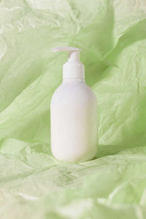 Lotion bottle skin care beauty cosmetic product on green crumbled paper. Shampoo, soap, hair conditioner blank empty mock upの写真素材