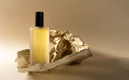 Perfume bottle and golden crumbled paper on beige backgroundの写真素材