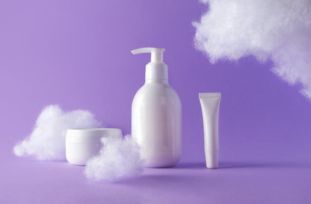 Cosmetic set with clouds on violet. Beauty products bottles for skincare or body care. Concept care with sensitive skin. Creative still-life photoの写真素材