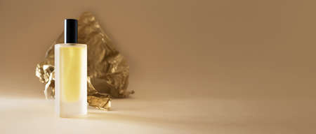 Perfume bottle and golden crumbled paper on beige background horizontal banner format with copy spaceの写真素材