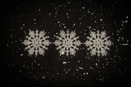 Three white glitter snowflakes on the black background.の写真素材