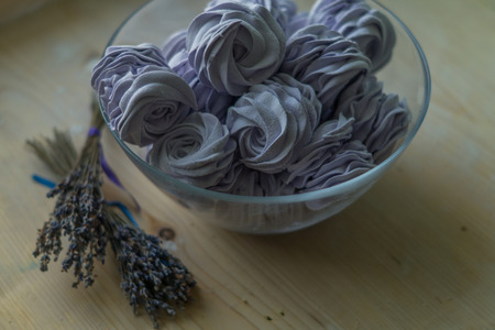 Violet marshmallow in a large glass bowl with lavender flowers in front,   stays on a wooden tableの写真素材
