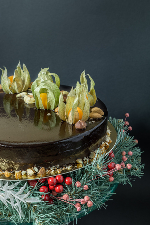 Holiday chocolate mousse cake with winter decoration on a stand of fir-tree with berries on a black backgroundの写真素材