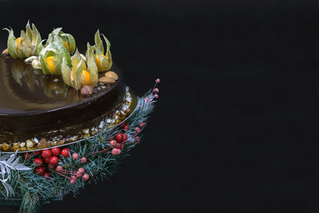Holiday or birthday chocolate mousse cake with decoration on a stand of fir-tree with berries on a black backgroundの写真素材
