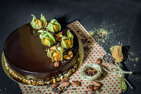 Birthday chocolate mousse cake with decoration, cocoa beans, almonds, anise and sugar, two spoons and thread on a black background and craft paper with red dots.の写真素材