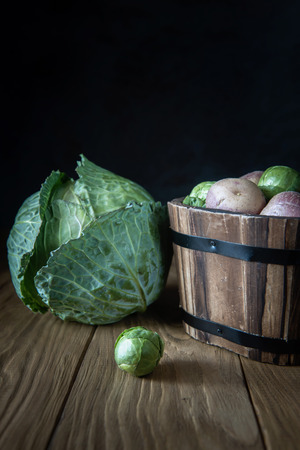 Selection of fresh garden vegetables (white cabbage, Brussels sprouts and pink potato tubers) on natural wooden background. Selective focus. Rustic style. Natural light. Copy space.の写真素材