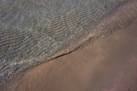 Small wave playing with pink toned sand of famous Elafonisi beach at Crete island, Greece. Wavy sand bottom can be clearly seen through clean water. Background with copy space.の写真素材