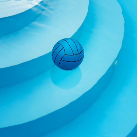 Square image of blue ball swimming alone on water surface in private pool. Stairs are visible through clean water with reflected surroundings. Summer atmosphere and private safety on water concepts.の写真素材