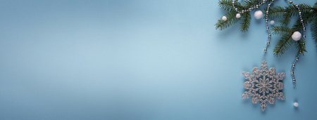 Festive banner with natural green fir branches, silver snowflake Christmas decoration, white artificial snowballs and silver colored chain on blue paper. Large copy space. Winter holiday concept.の写真素材