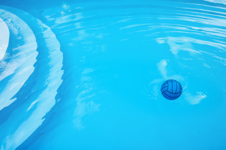 Child's blue ball, circles and air bubbles on water surface in pool.  Stairs are visible through...