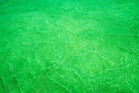 Empty abstract background naturally created by small sea waves in shallow waters and sunlight reflections on water surface. Toned in shades of electric green. Copy space. View from above.の写真素材