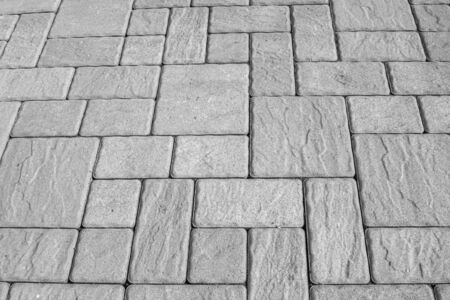 Geometric horizontal monochrome background with artificial stone paving made of square blocks of different shapes and sizes. Perpendicular and parallel lines. High angle view. Black and white image.の写真素材