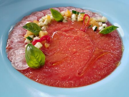 Close-up of restaurant served refreshing Spanish gazpacho soup made of red tomatoes, served in white plate and decorated with fresh vegetables and basil leaves. Healthy eating and dieting concept.の写真素材