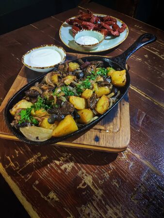 Baked golden potato wedges served with wild mushrooms in black cast iron frying pan, accompanied by...