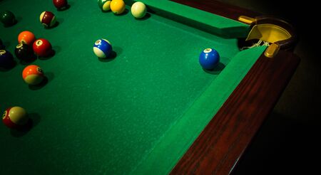 Few colorful numbered balls on green table, near its corner and ball pocket.. Horizontal background with equipment for Americal billiard cue sport game, leisure and hobby activity. Copy space.の写真素材