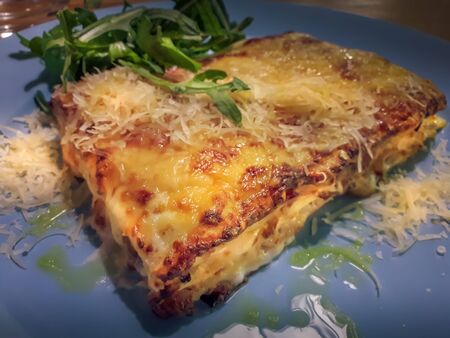 Large portion of traditional italian lasagne covered by crust of melted parmesan cheese. It is...