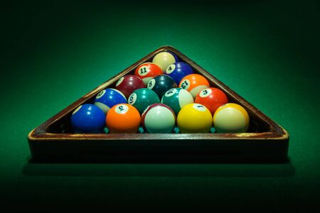 Group of colorful numbered balls in wooden triangle on green table. Horizontal background with equipment for American billiard cue sport game, leisure and hobby activity. Copy space.の写真素材