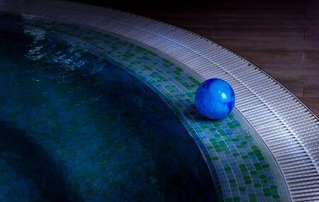 Blue ball is left on side of swimming pool decorated with mosaic tiles. Stairs are visible through shallow water. Summer season and private safety on water concepts. Selective focus. Copy space.の写真素材