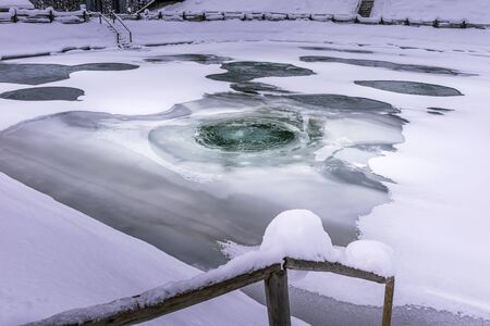 Aerated fish pond in winter. Ice covering the pond is melting, because of aeration process, so fish population is protected. Horizontal seasonal background with environmental protection concept.の写真素材