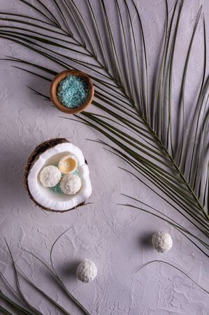 Flat lay with half of coconut in shell, coconut flakes in bowl, coconut candies and palm leaves on white textured table surface. Coconut is filled with blue coconut flakes and white coconut candies. の写真素材