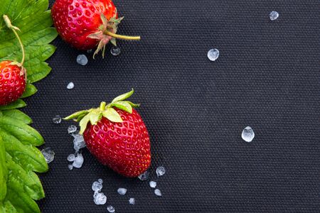 Red strawberries with few white hailstones and strawberry leaf on black textile material used for cultivating this berry in garden. Horizontal background with large copy space. Healthy eating concept.の写真素材