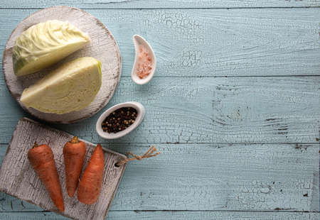 Background with set of cabbage fermenting ingredients. Cabbage, carrot, pepper and himalayan salt on white  cutting boards and on blue wooden table. Flat lay with copy space. Healthy food concept.の写真素材