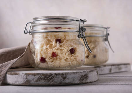 Glass jars full of fermented cabbage with red cranberries and linen napkin on side. Jars are on...