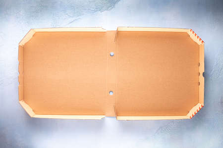 Whole new clean brown opened empty pizza box made of paperboard on blue stone textured background...