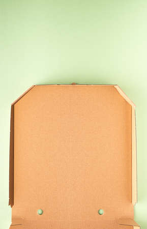 Part of new clean brown opened empty pizza box made of paperboard on light green or mint paper...