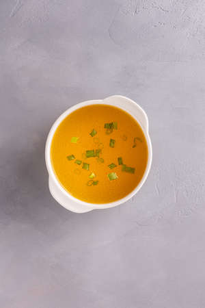 Bouillon in white soup bowl on gray stone table background. Chopped spring onions or scallions in bouillon. Directly above view. Vertical background with copy space. Healthy eating and dieting conceptの写真素材