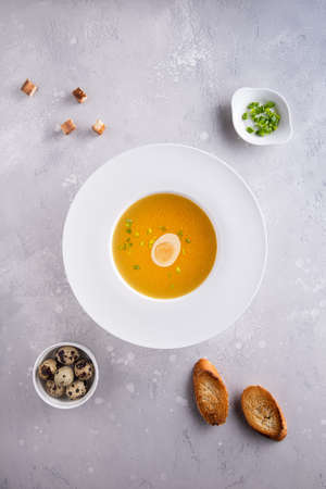 Bouillon in white soup plate, chopped spring onions or scallions, quail eggs, toasted bread and croutons on gray background. Flat lay. Vertical orientation. Homemade healthy eating and dieting conceptの写真素材