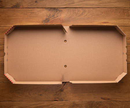 Mock up or template with new clean opened empty pizza box made of paperboard on natural wooden brown background. Horizontal orientation. Copy space. Home delivery and stay home concept.の写真素材