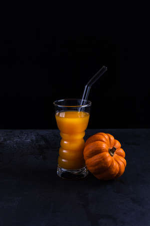 Pumpkin non-alcoholic mocktail in drinking glass with glass straw and whole orange pumpkin on black textured stone table surface. Healthy eating concept. Vegan and vegetarian food. Copy space.の写真素材