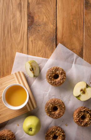 Baked apple cider donuts with apple cider and fruits on baking sheets on natural wooden table. Ready to eat snack. Small batch of homemade food. Directly above view. Vertical orientation. Copy space.の写真素材