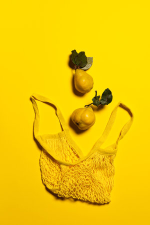 Two quince apples and yellow mesh bag on yellow background. Directly above view. Fruits and leaves have natural imperfections, spots and scratches. Eco friendly shopping and sustainable living conceptの写真素材