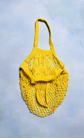 Bright yellow empty mesh bag on blue textured concrete background. Flat lay. Vertical orientation....