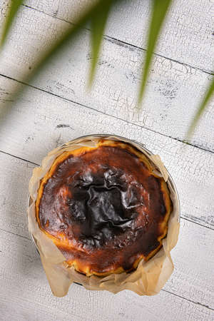 Homemade basque burnt cheesecake in baking paper and baking tin on textured white wooden table....