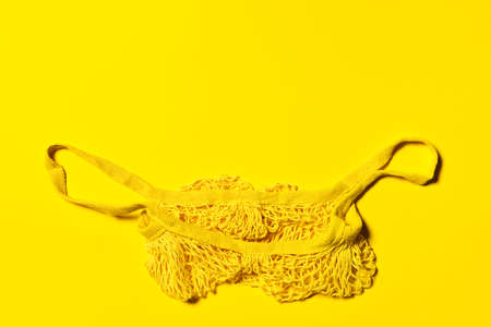 Bright yellow empty net shopping bag on yellow paper background. Flat lay. Horizontal orientation. Conscious consumerism and eco friendly shopping concept. Large copy space.の写真素材