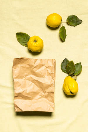 Flat lay with three yellow organic quince apples and used paper shopping bag on wrinkled pastel colored linen background. Fruits have natural imperfections. Conscious consumerism concept.の写真素材