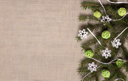 Fir branch with green rattan balls, white wooden snowflakes and raffia on beige linen material. Flat lay with natural recyclable decorative elements. Eco friendly winter holidays concept. Copy space.の写真素材