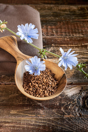 Heap of Instant granules and blue chicory flower in wooden spoon on rough brown natural wooden plank table with cracks. Linen textile napkin and plant stem in bloom on side. Vertical orientation.の写真素材