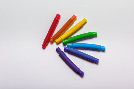 Group of new straight rainbow colored red, blue, orange, purple, green and yellow pop tube children toys. Cheerful plastic antistress multicolored tubes on white textured paper background. Flat lay.の写真素材