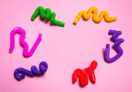 Colorful red, purple, pink, green and yellow pop tube children toys bent in different shapes. Cheerful plastic antistress multicolored toy set on pink paper background. Flat lay. Copy space in centre.の写真素材
