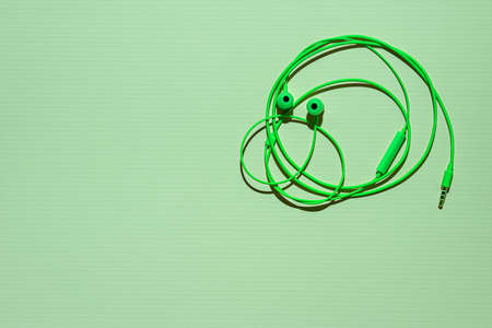 Bright green earphones with microphone and 3,5 mm mini-jack connector on green textured paper background. Wire in shape of funny round face of human with eyes and nose. Large copy space. Flat lay.の写真素材