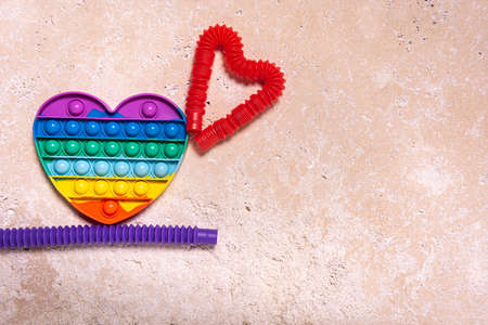 Stretched purple and red pop it tube children toys bent in different shapes and rainbow heart. Plastic antistress multicolored toy set on natural travertine stone background. Flat lay. Copy space.の写真素材