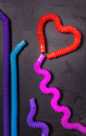 Red heart made of tube, straight and bent as waves pink, blue and purple pop tube toys. Plastic antistress multicolored toy set on black textured concrete background. Flat lay. Valentine concept.の写真素材