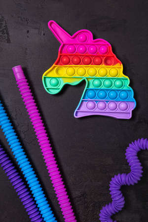 Stretched straight and bent as wave pink, blue and purple pop tube children toys and rainbow popping toy unicorn. Plastic antistress multicolored toy set on black textured concrete background. Flat lay.の写真素材