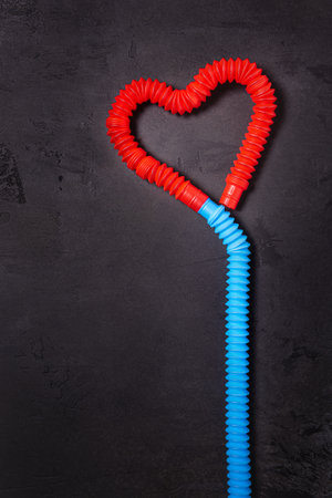 Red heart and blue, bent as ribbon pop tube toys. Plastic antistress multicolored children toy set on black textured concrete background. Flat lay. Valentine concept. Copy space. Vertical orientationの写真素材