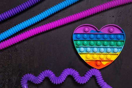 Flat lay with stretched straight and bent as wave pink, blue and purple pop tube children toys and rainbow popping toy heart. Plastic antistress multicolored toy set on black textured concrete background.の写真素材