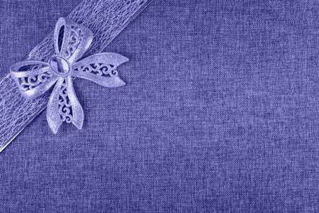 Elegant shiny tied glittering bow and ribbon on natural burlap. Image toned in very peri, color of year 2022. Horizontal background with Christmas decor in corner and large copy space. View from aboveの写真素材